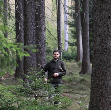 a man in a black jacket is standing in a forest