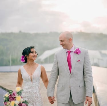 A smiling bride and groom holding hands while walking outdoors during a tropical destination wedding.