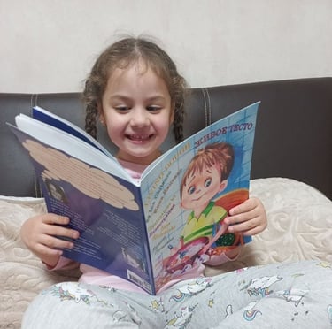 7-year-old girl reads Living Dough by Ina Chitenco on her bed, smiling and captivated by the story.