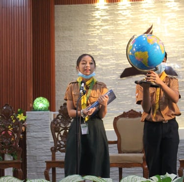 2 elementary scout students with a book and globe speaking on a stage
