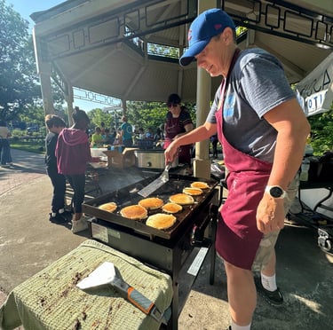 Kids in the background of a person flipping pancakes on a griddle in a park