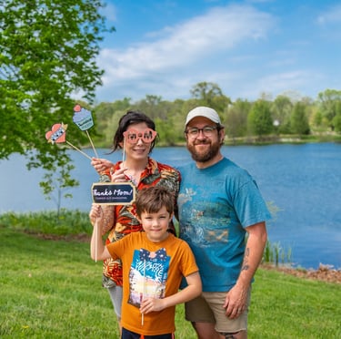 Staged photo of a couple with a young child in front of a lake, holding up paper props