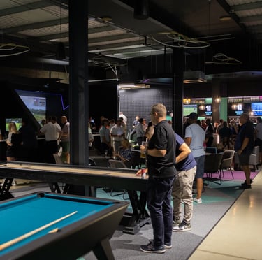 A busy event at 1IRON indoor golf simulator venue with people playing pool, shuffleboard and golf