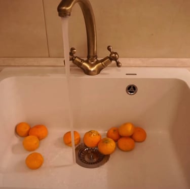 Film still from The Wait by Tina Bikic showing oranges in a white sink under running water from a brass tap.