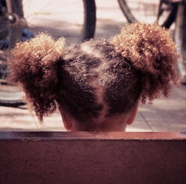 Little mixed race girl with curly hair sitting on a bench