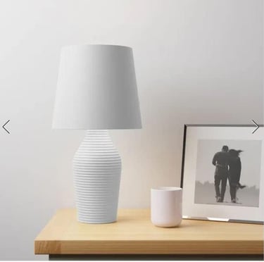 Modern white ribbed ceramic table lamp with fabric shade on a wooden nightstand.