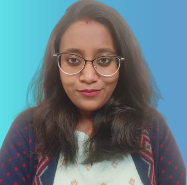 Professional portrait of an Indian woman wearing glasses and a patterned sweater against a blue background.