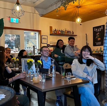 A diverse group of friends laughing and enjoying drinks at a cozy bar with industrial pendant lighting.