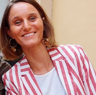 Smiling woman with short brown hair wearing a red and white striped linen blazer and gold hoop earrings.