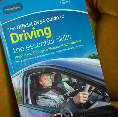 The Official DVSA Guide to Driving the Essential Skills book with car keys on a yellow chair.