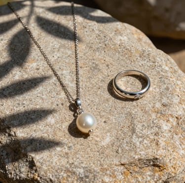 A beautiful aesthetic shot of jewelry pieces laid out on a textured sand-colored stone, with shadows of leaves, capturing the quiet elegance of Breton nature.