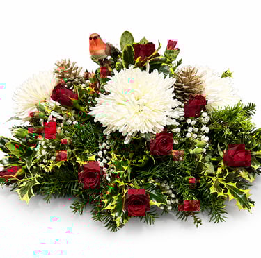 Christmas floral centerpiece with red roses, white chrysanthemums, holly, and a robin figurine.