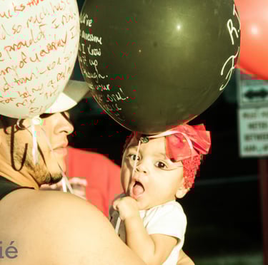 baby with red hair bow being held by father in the middle of a sea of balloons