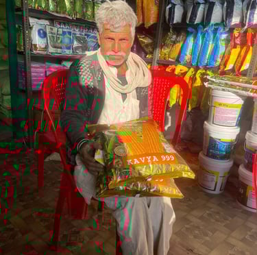 Indian farmer sitting in a supply store holding bags of Kavya 999 hybrid corn seeds.