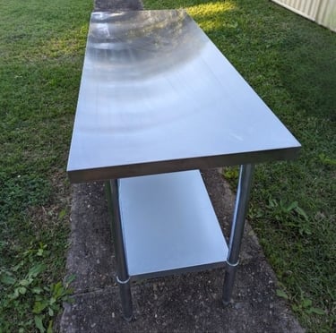 Table Hire: Long stainless steel workbench with undershelf, ideal for outdoor events.