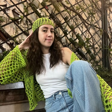 A woman posing on a bench, wearing her stylish green croquet long sleeved top and beanie. 
