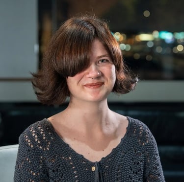 A smiling woman with a short auburn bob haircut wearing a grey crochet cardigan.