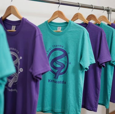 A bright display of custom-designed t-shirts featuring unique screenprints in vibrant turquoise and purple hues on a clean hanger.