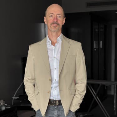 Portrait photo of Mark Murfitt wearing a cream colored jacked, white shirt, black jeans