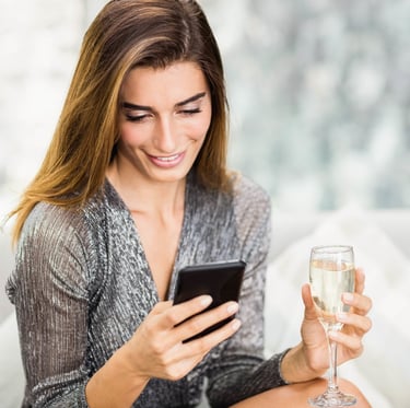 Jolie jeune femme tenant dans sa main gauche une flûte de Champagne et dans l'autre un téléphone
