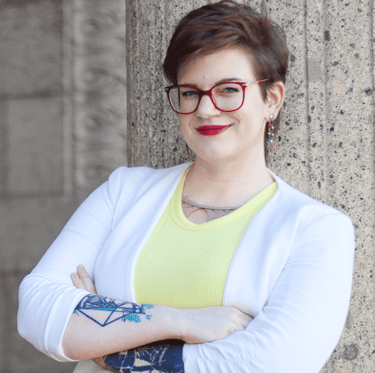 a photo of Swana Schuchmann with short hair, a white blazer and glasses, smiling