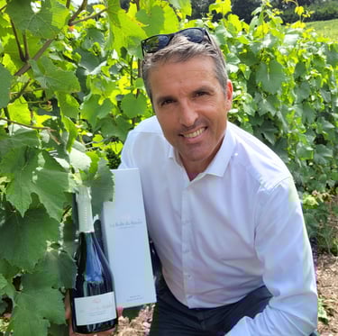 Patrice agenouillé dans les vignes tenant une bouteille de Champagne La Bulle du Bassin et son étui