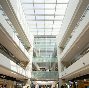 Symmetrical wide-angle architectural photography of a modern commercial mall interior in Kuala Lumpur, bright natural daylight streaming through glass atrium, clean high-contrast corporate tones, sharp details