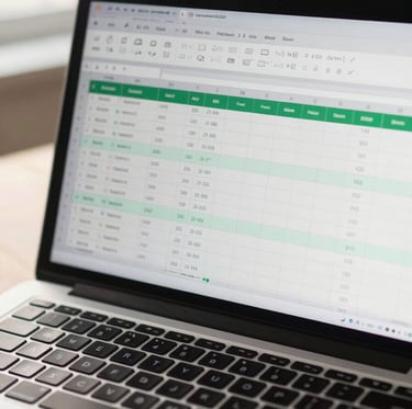 Overhead wide shot of a modern laptop screen displaying a clean Excel dashboard with green-tinted data cells, formula bar visible, soft natural light from the left, keyboard partially in frame, slight lens warmth