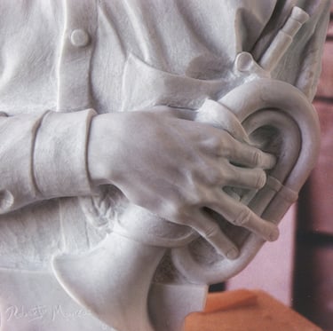Hand-carved white marble bust of a young man holding a bugle in a workshop setting.