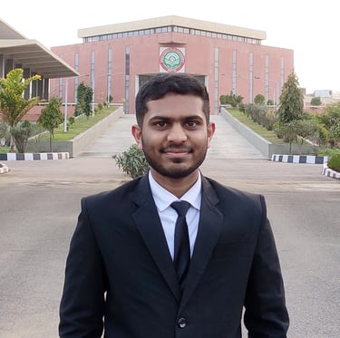 A man in a black suit standing in front of a modern building with a green and red logo. The well-maintained path leading up t
