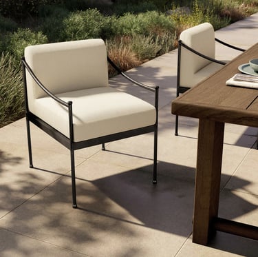 Modern black metal outdoor dining chairs with cream cushions on a stone patio by a wooden table.