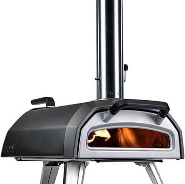 A portable outdoor wood-fired pizza oven with a stainless steel chimney and a glowing flame inside.
