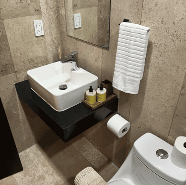 Baño con lavamanos cuadrado, espejo minimalista y recubrimiento de piedra natural beige | KARÄNA