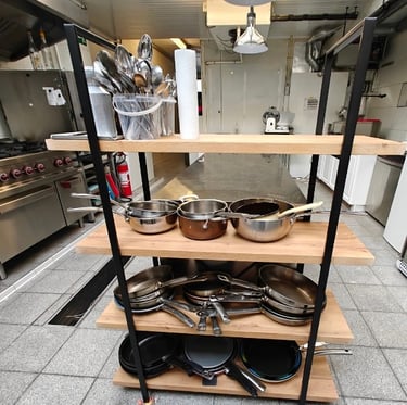 Organised shelving unit with professional stainless steel and copper pans in a restaurant kitchen