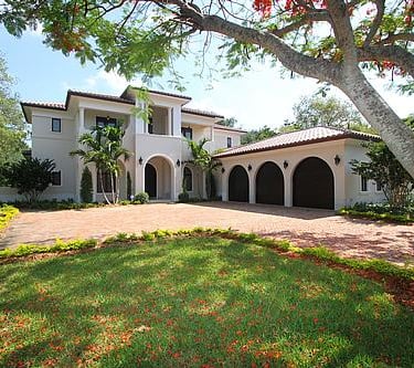 spanish style luxury home with an L shaped driveway and trees and red flowers and autumn leaves