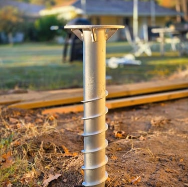 A galvanized steel ground screw pile installed in dirt for a backyard deck foundation.