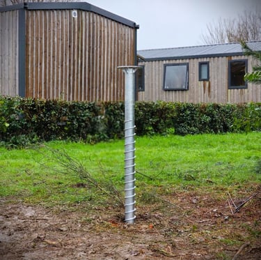 Galvanized steel ground screw foundation installed in a grassy yard for eco-friendly building construction.
