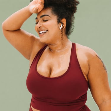 A smiling, sweaty plus size brown woman with curly hair in a red sports bra resting after a workout.