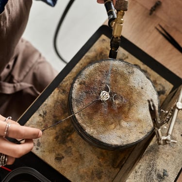 Joyero con un soplete de gas para soldar un anillo de plata en un bloque de soldadura en un taller.