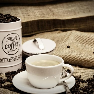 A professional image of an overflowing canister of coffee beans and a cup of milky coffee on an empty hessian bag