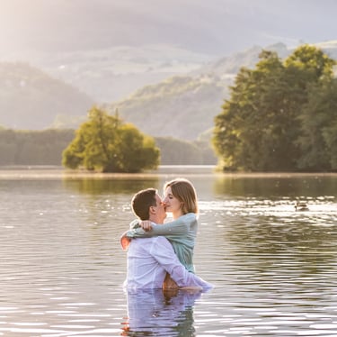 un couple enlacé dans un lac avec des montagnes en arrière plan au coucher du soleil