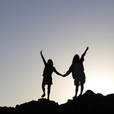 2 silhouettes de femmes qui se tiennent la main sur le haut d'une colline et qui regarde l'horizon