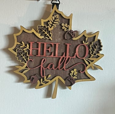 Leaf-shaped wooden wall sign saying "Hello Fall" with acorn and leaf accents.