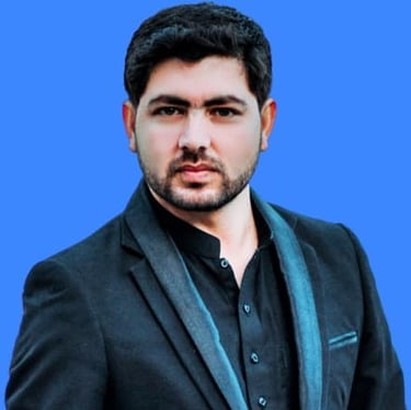 Professional portrait of a bearded man in a black blazer and traditional shirt against a blue background.