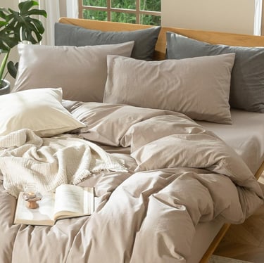 Neutral beige linen bedding set on a wooden frame with grey pillows and a cozy knit throw.