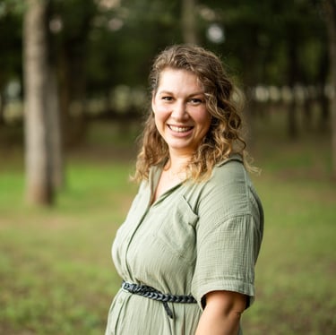 Headshot of Meg Gigl in a green dress with tress in the background