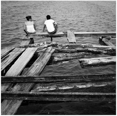 Honduras: two people sitting on a dock with a boat in the water