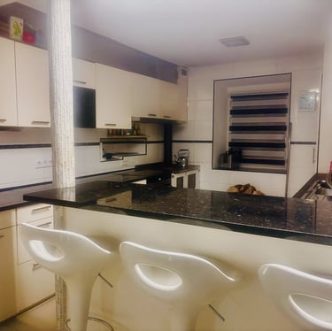 Cuisine moderne avec comptoir en granit noir, armoires claires et tabourets blancs.