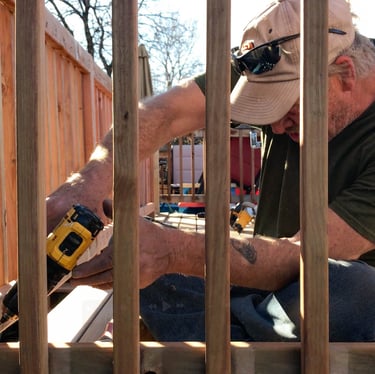Brewer Construction carpenter installing new deck balusters on an Evergreen property with a power drill.
