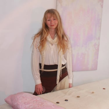 Reiki practitioner smiling in a calm healing room with a treatment table and pastel artwork